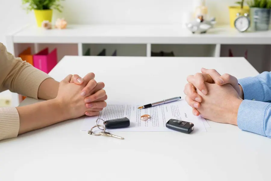 Two people at a table with a pen, rings and car keys on a document